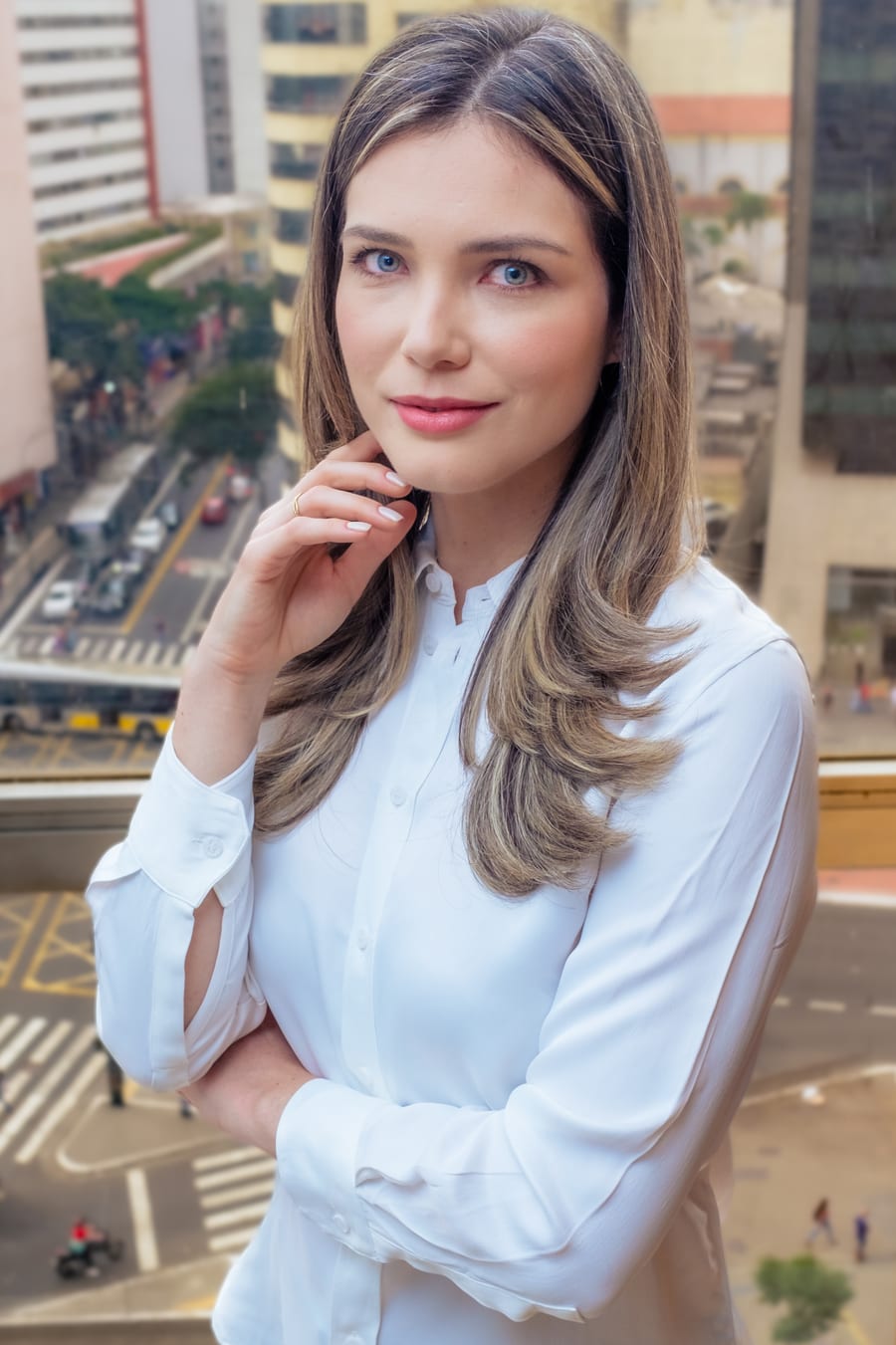 Dra. Renata Müller Couto em frente à janela do consultório, com a cidade de São Paulo ao fundo