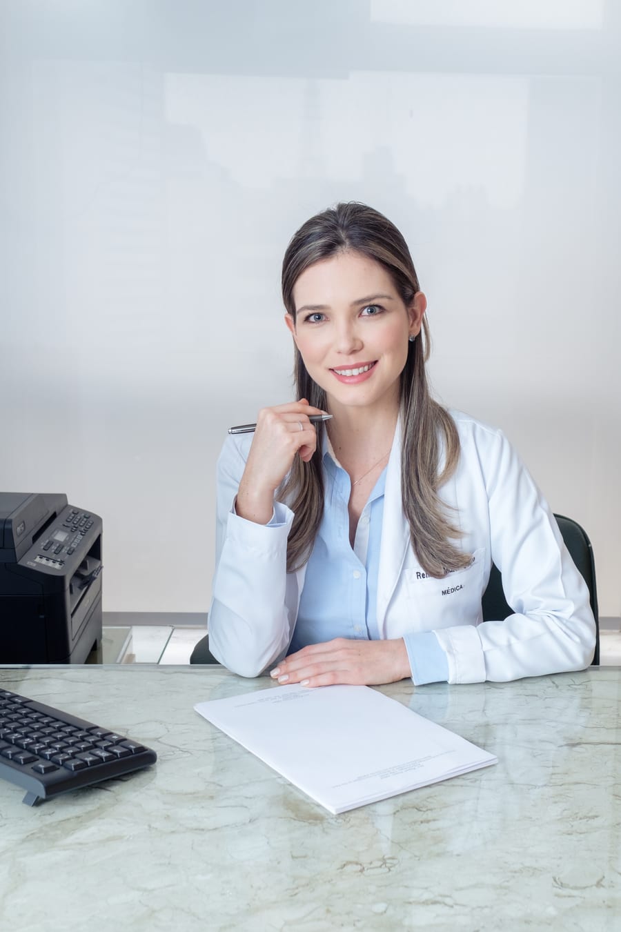 Dra. Renata Müller Couto sentada à mesa do consultório, sorrindo durante o atendimento